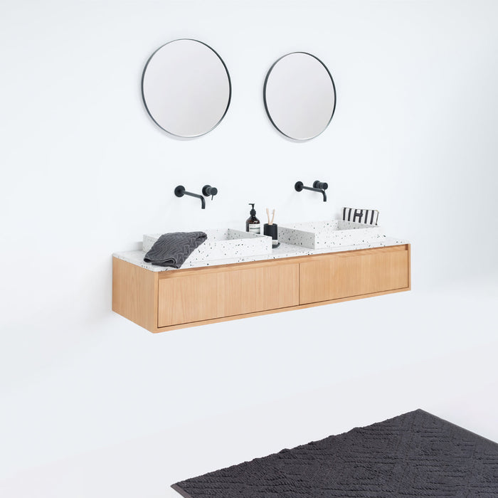 ronde grote spiegels, zwarte moderne kranen, zwevend badkamermeubel in eikhout en wit terrazzo wastafelplaat en lavabo